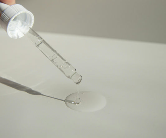 Dropper releasing a drop of retinol serum onto a pale surface
